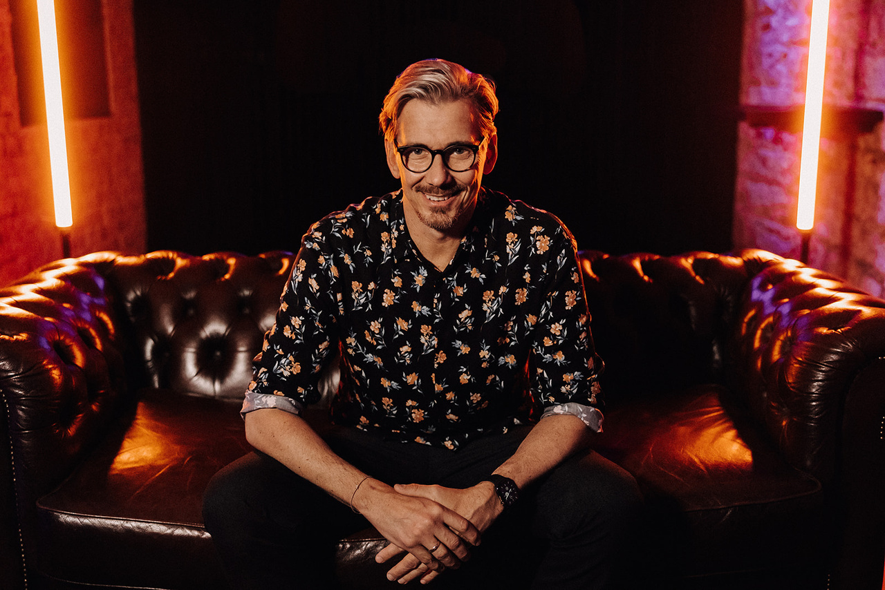 Portrait von Alex Maus auf einem Chesterfield-Sofa, warmes Neon-Licht
